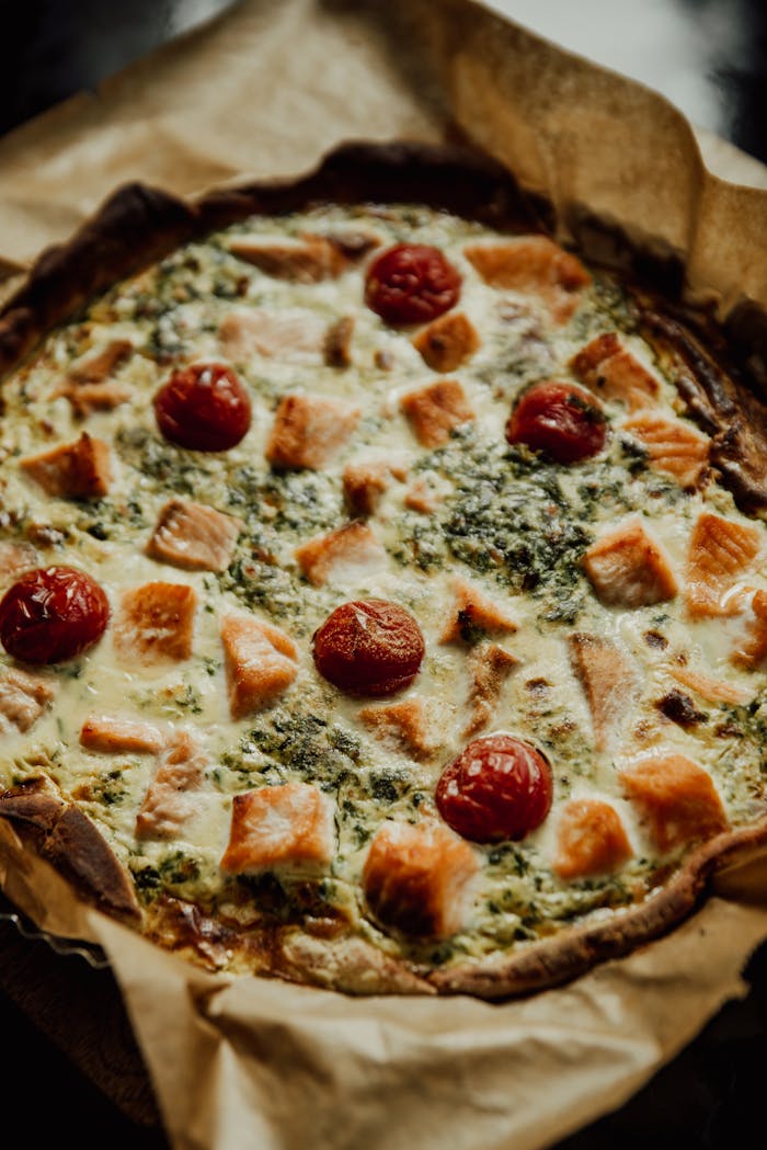 Delicious quiche topped with chunky salmon, cherry tomatoes, and spinach, perfect for a flavorful meal.